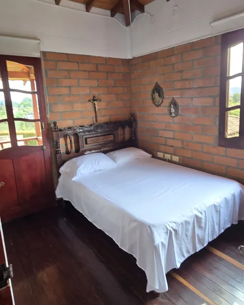 Habitación principal con cabecero tallado, muro de ladrillo y piso de madera