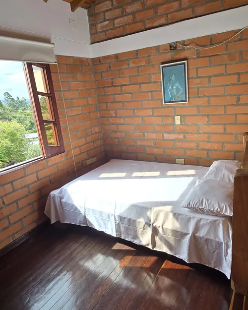 Habitación de muros en ladrillo con cama sencilla y ventana al jardín
